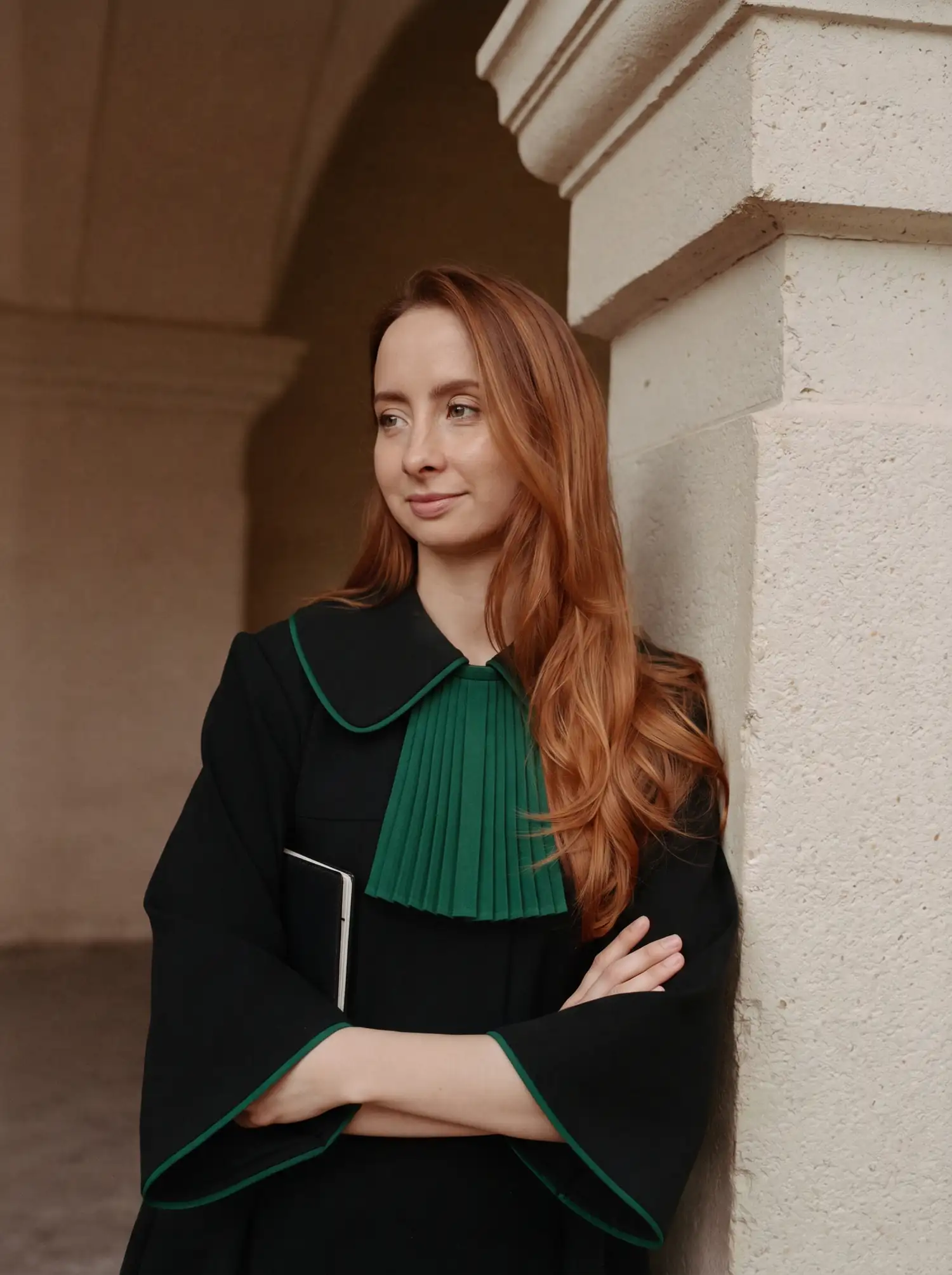 Adwokat Zuzanna Rączkowiak-Dobrowolska w todze, oparta o kamienny filar pod arkadami